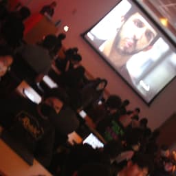 a room illuminated in red light of people watching a person on the projector